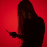 Silhouette of a woman with braids focused on her cellphone against a red background.