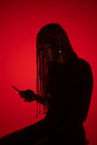 Silhouette of a woman with braids focused on her cellphone against a red background.